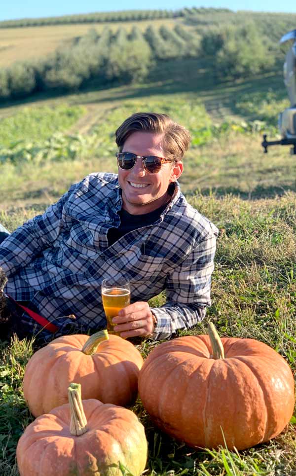 A man posing with pumpkins while drinking wine.