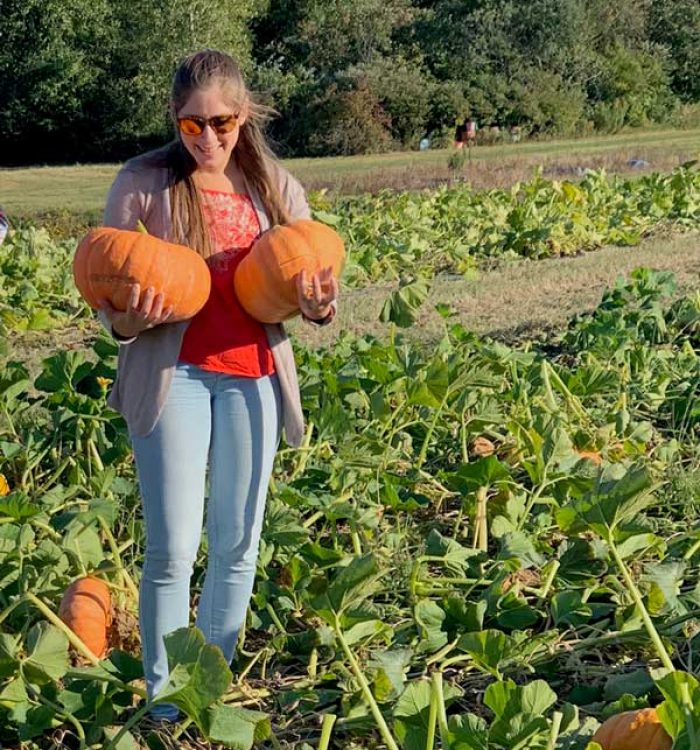 A woman holding pumpkins in a pumpkin patch